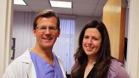Dr. Guy McKhann and patient Kelly Rolo stand next to each other holding her marathon bib, which says "ThxMcKhann"
